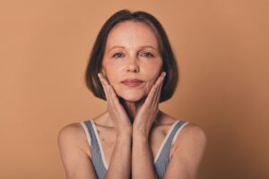 Woman in her 60s frames her face with her hands, highlighting areas of volume loss before micro-fat transfer