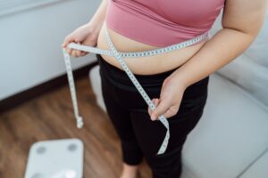 A woman, happy with her weight loss but unhappy about loose skin, holds a tape measure around her waist before RF skin tightening