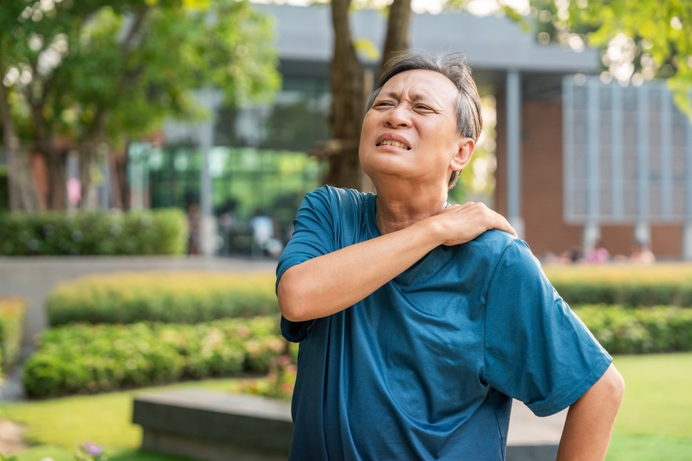 Man with chronic neck pain grabs his shoulder and neck and winces before a Botox treatment